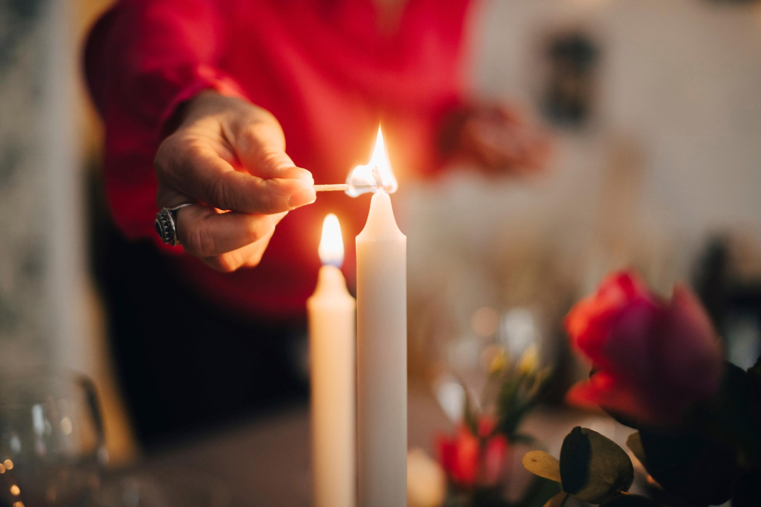 A candle is lit by a person in a red jumper.