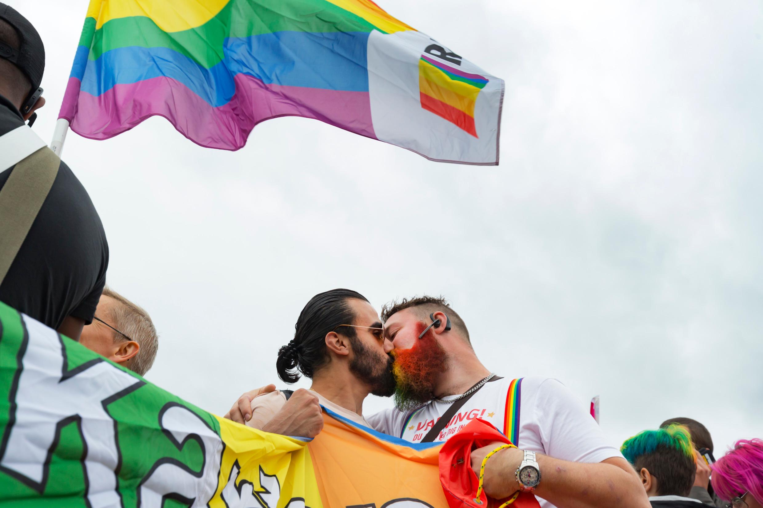 Two men kissing under a rainbow-coloured flag. LGBTQI rights are part of openness in Sweden.