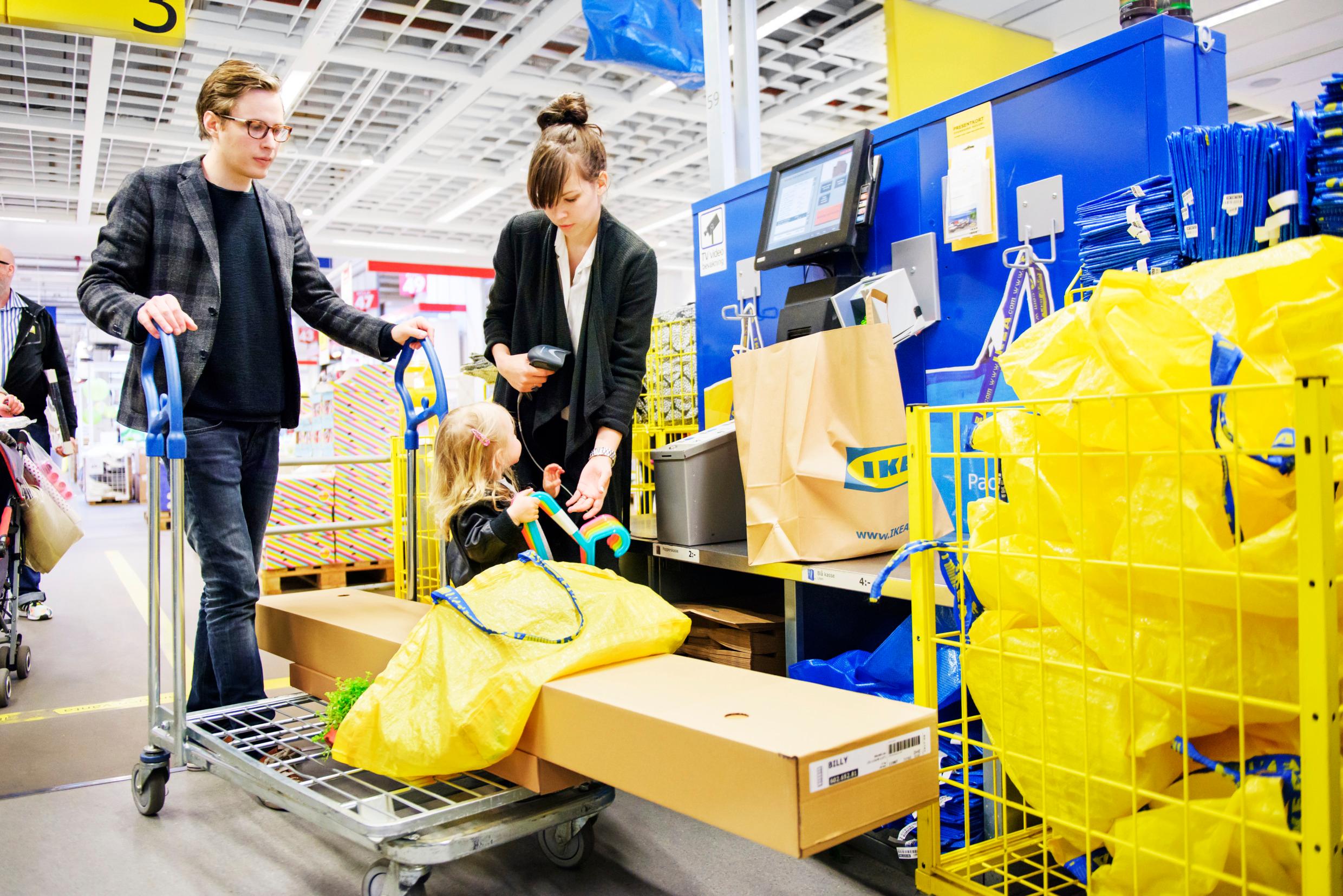 A man and a woman pushing a big cart with a cardboard and a yellow bag on.