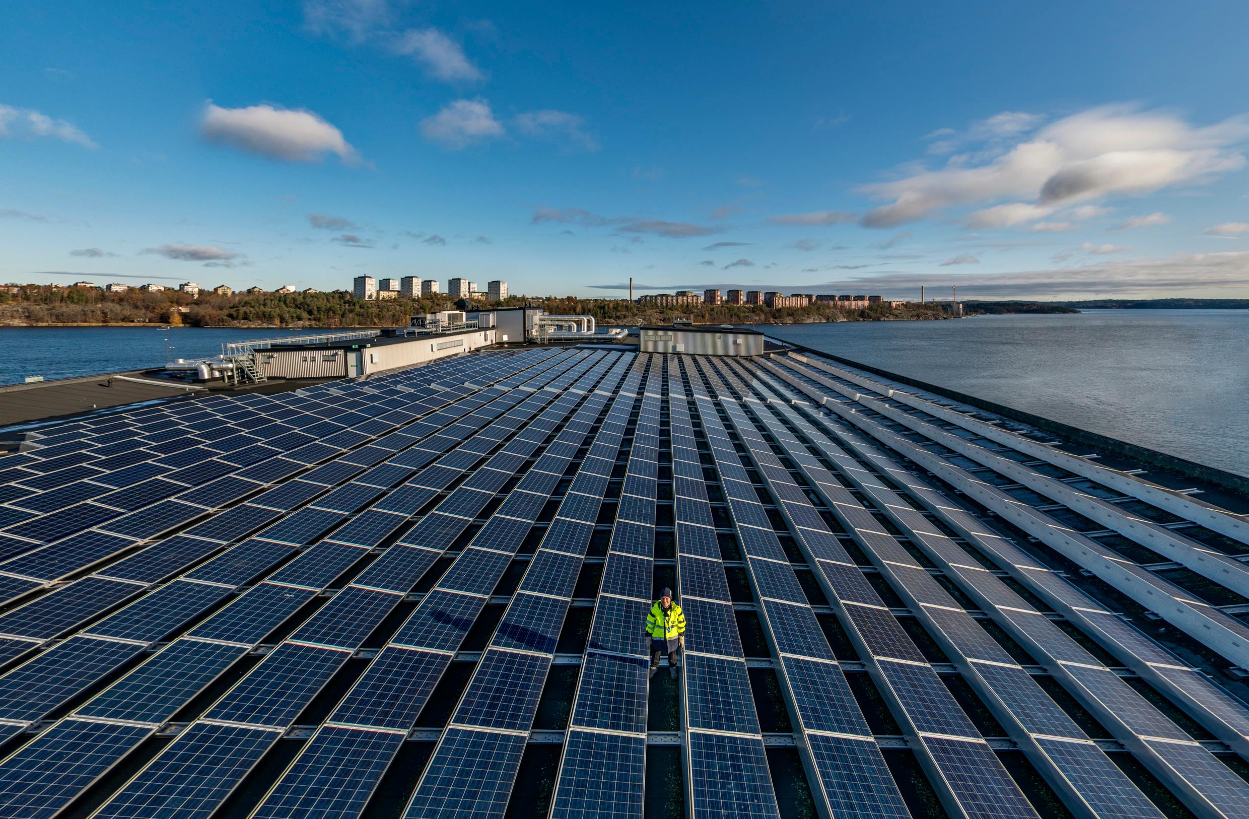 A huge rooftop solar energy facility with a large body of water and a city in the background.