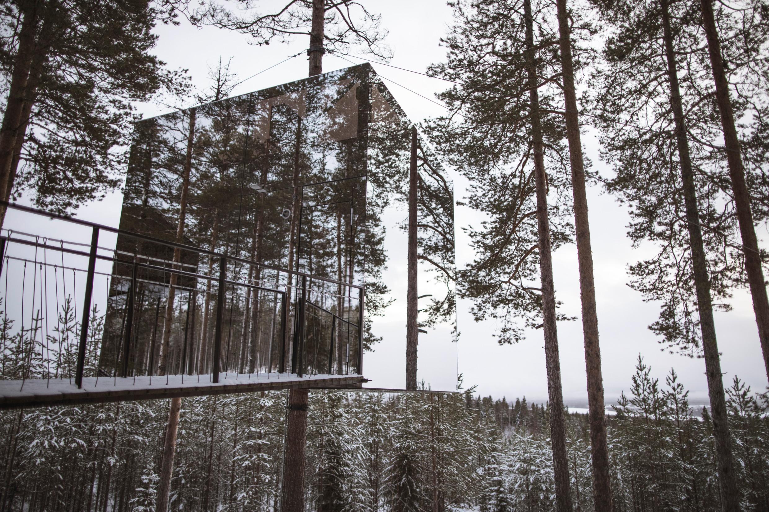 A treehouse made of mirror glass, set in a snowy forest in Swedish Lapland.