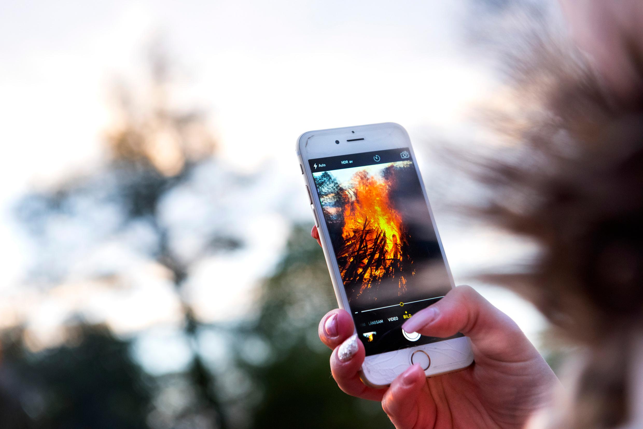 A hand holding a phone with a Walpurgis bonfire showing on the screen.