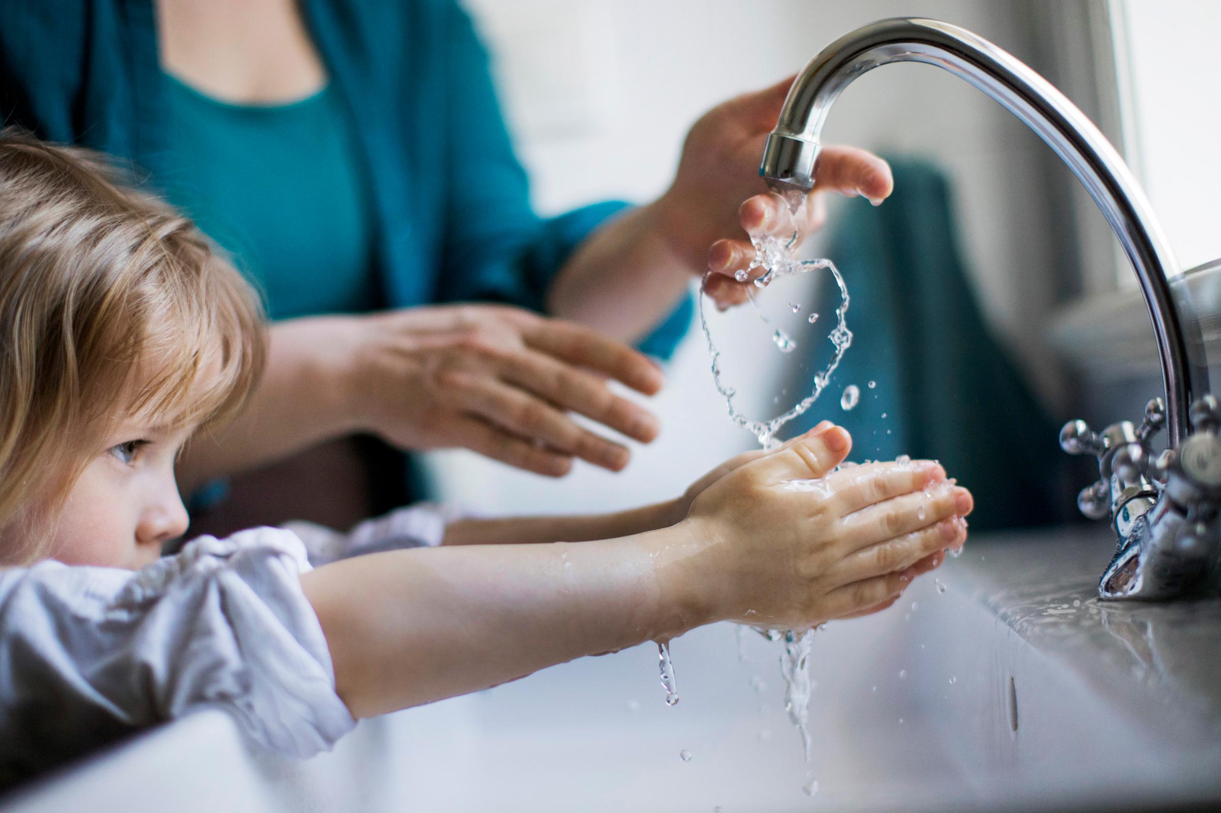 A young girl is washing her hands under a running faucet.