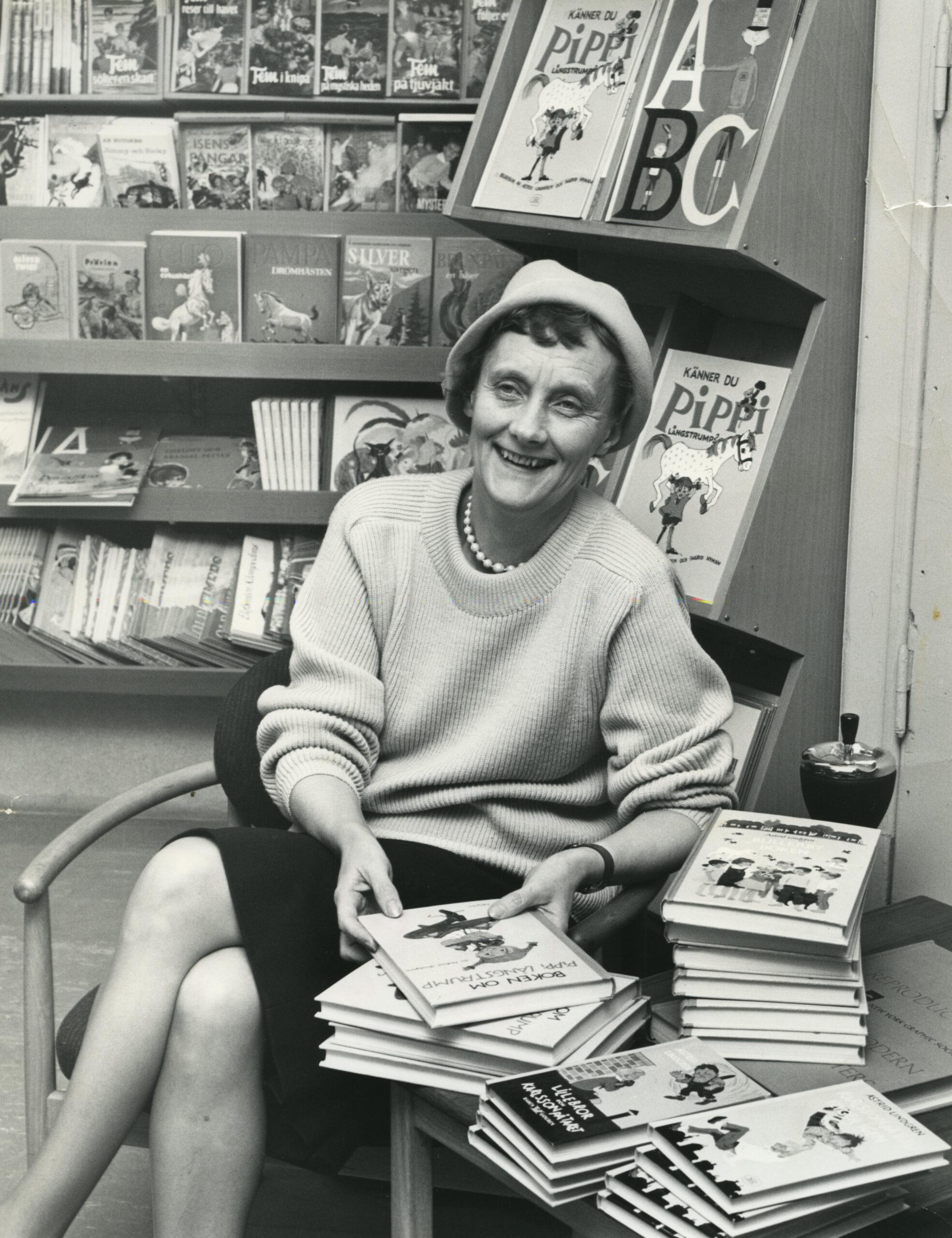 A black-and-white photo of Astrid Lindgren sitting at a table with lots of books on.