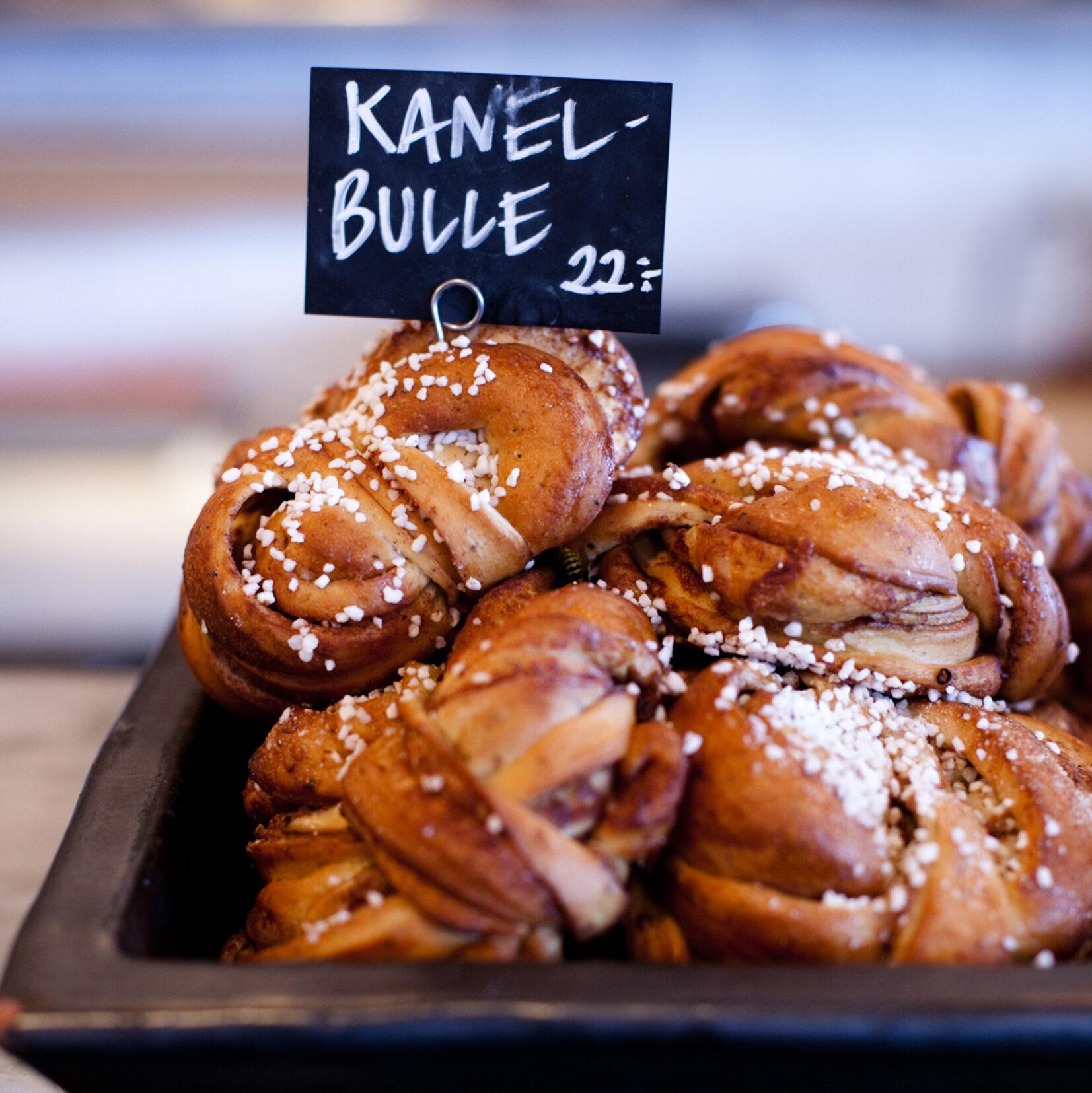 A tray of cinnamon buns on display with a handwritten sign reading 'Kanelbulle 22' which is the name for cinnamon bun in Swedish and the price. 'Kanelbulle' is an important part of the Swedish glossary.