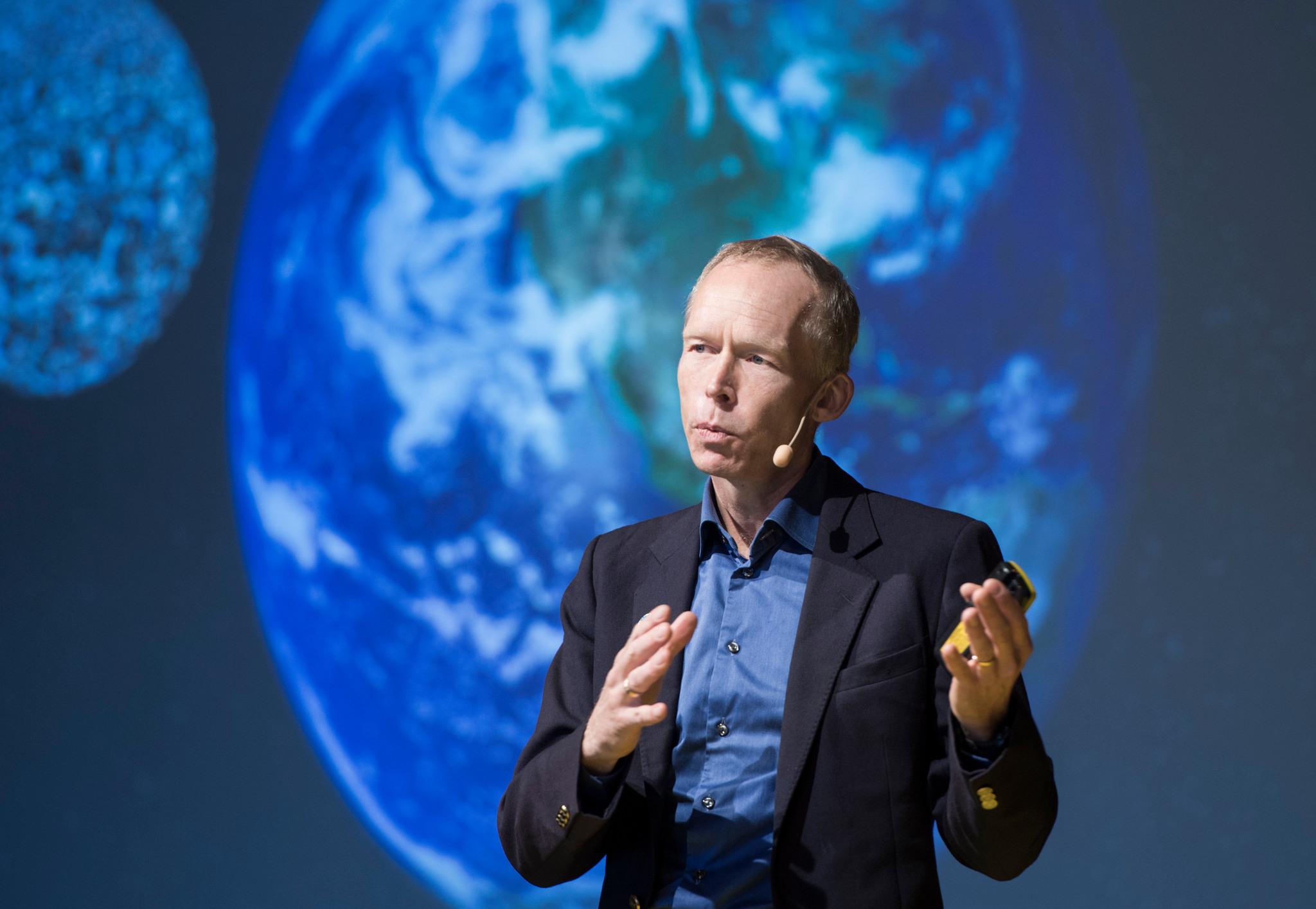 Professor Johan Rockström is gesticulating with his hands while speaking. Behind him is a blurred picture of Earth