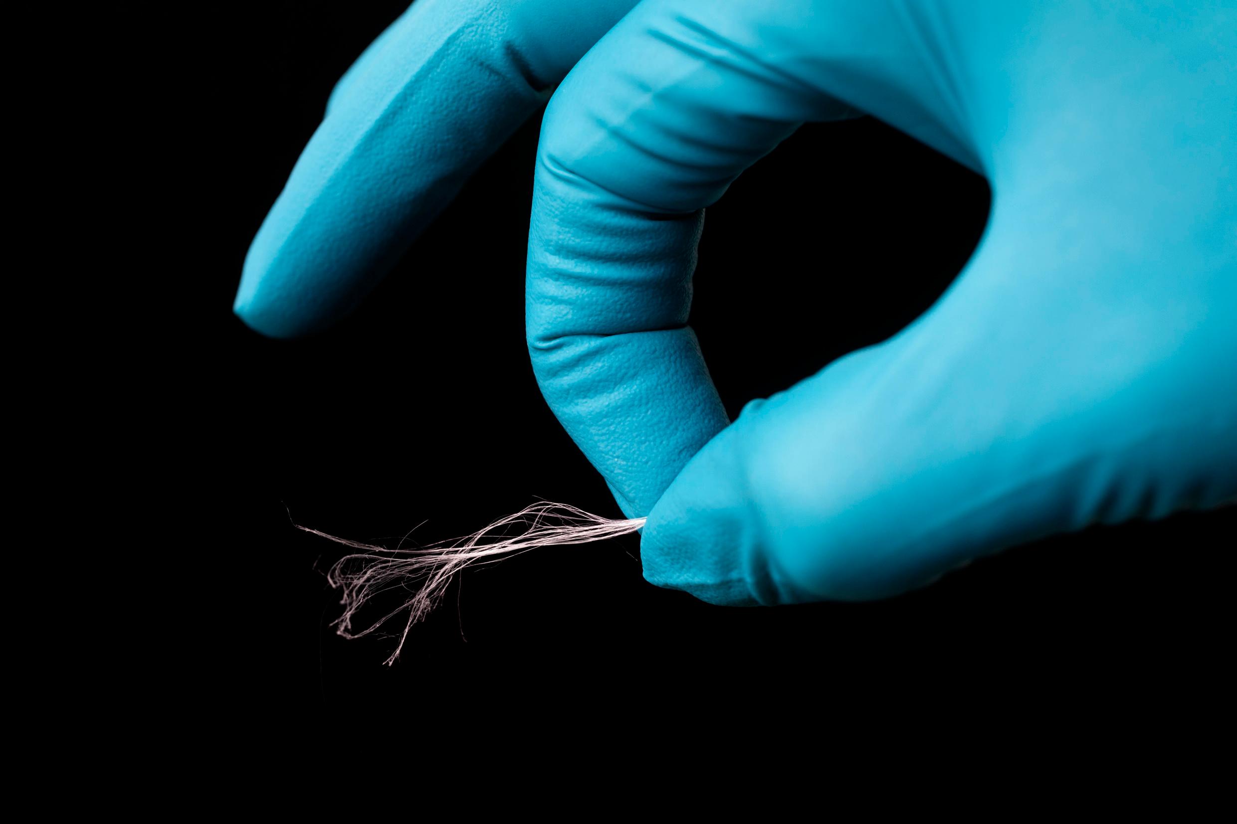 A hand covered with a latex glove holds up a very thin thread.
