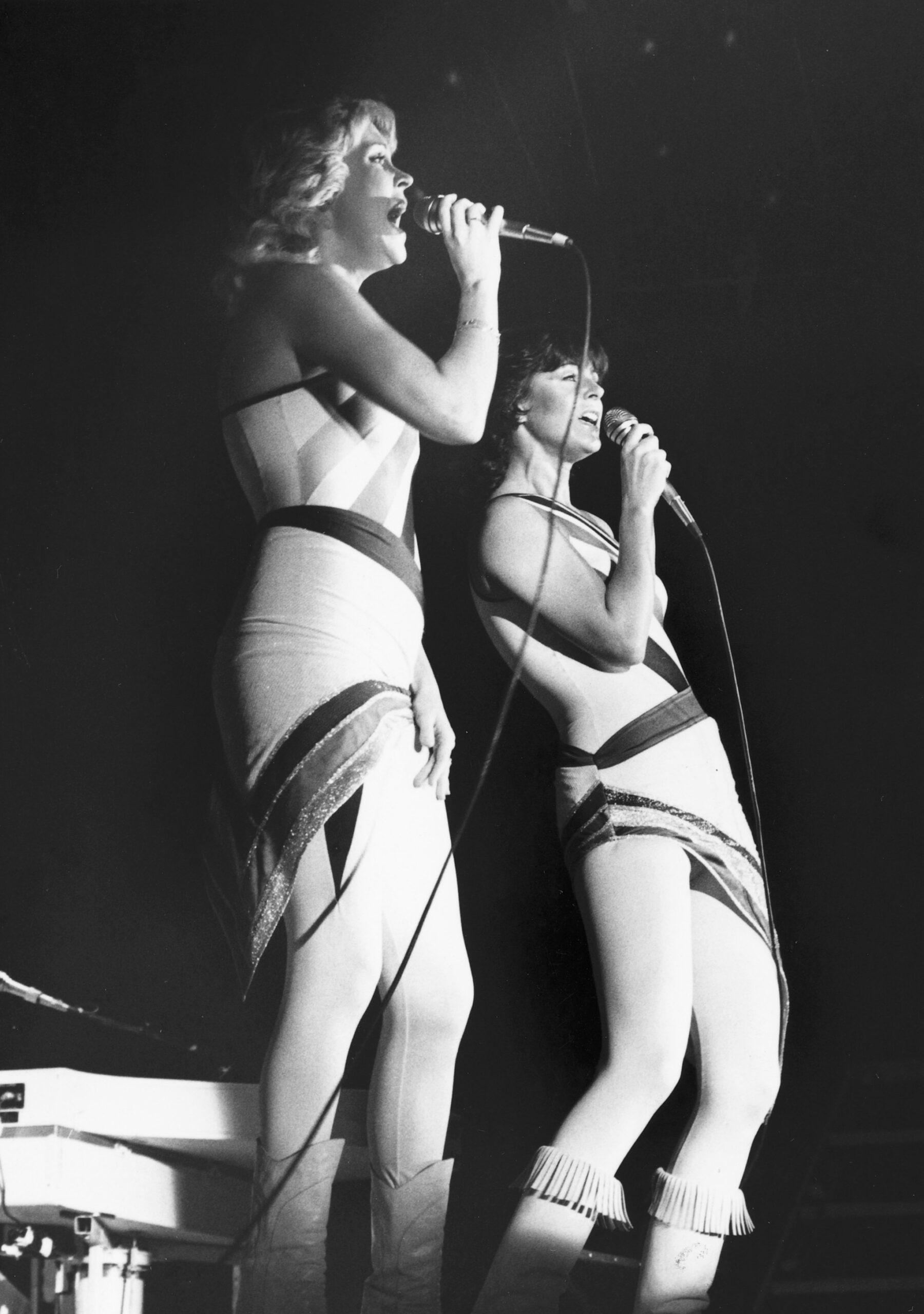A black-and-white photo showing ABBA's Agnetha Fältskog and Anni-Frid Lyngstad singing on stage.