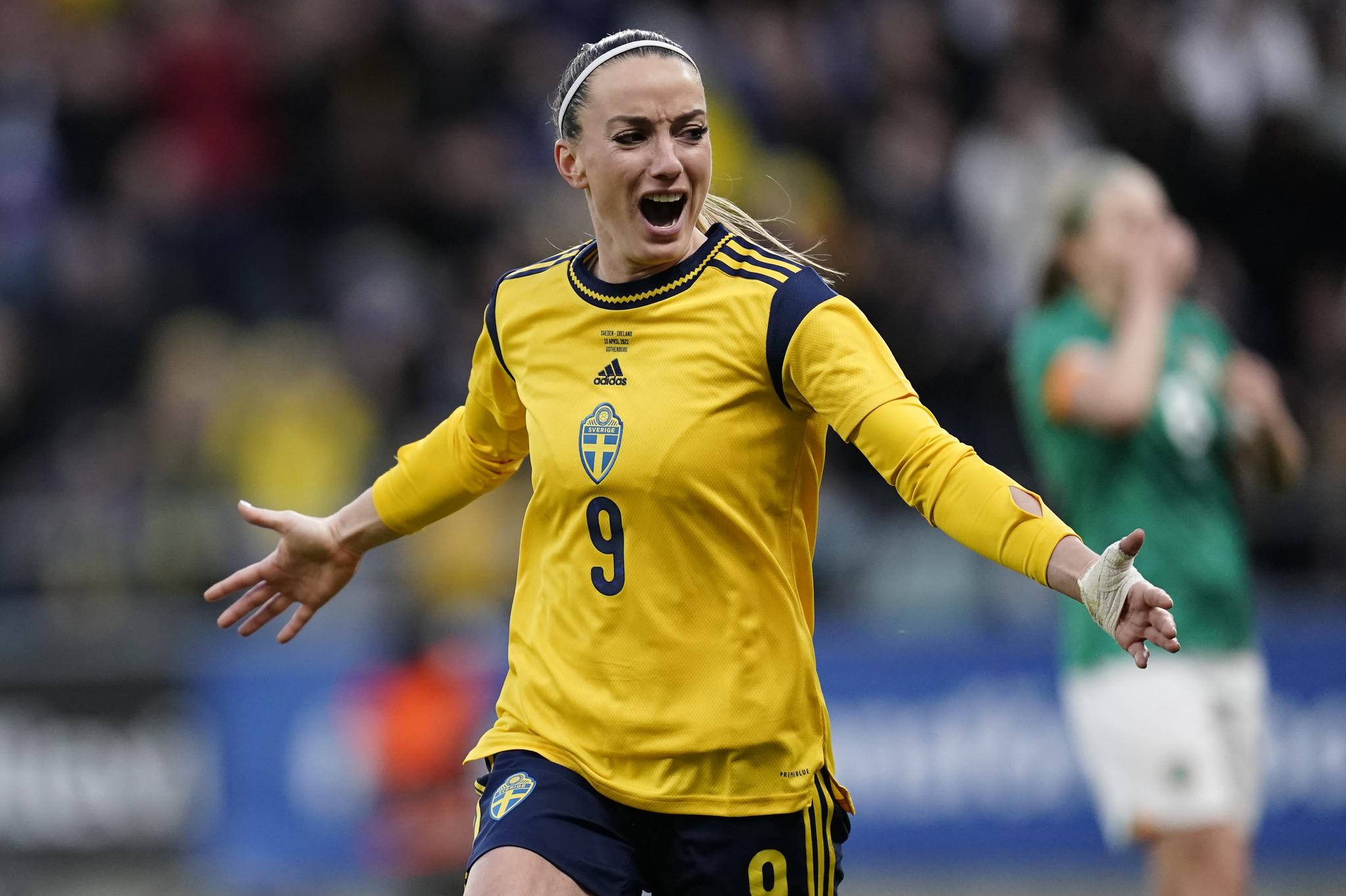 Footballer Kosovare Asllani dressed in Sweden's national team colours jubilant after scoring, running with her arms stretched out.