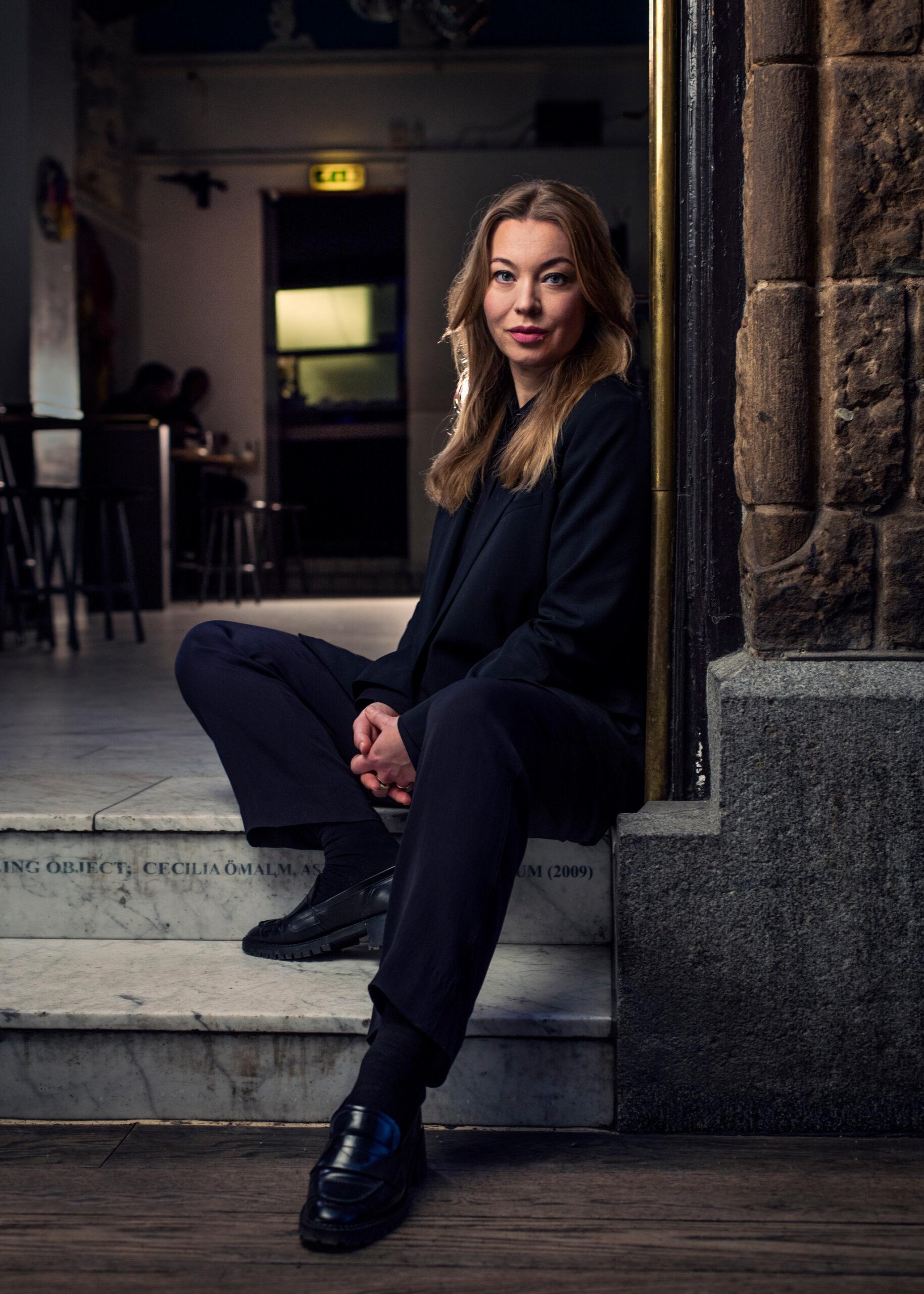 Portrait photo of Karolina Ramqvist sitting on some steps. She is wearing a dark suit.