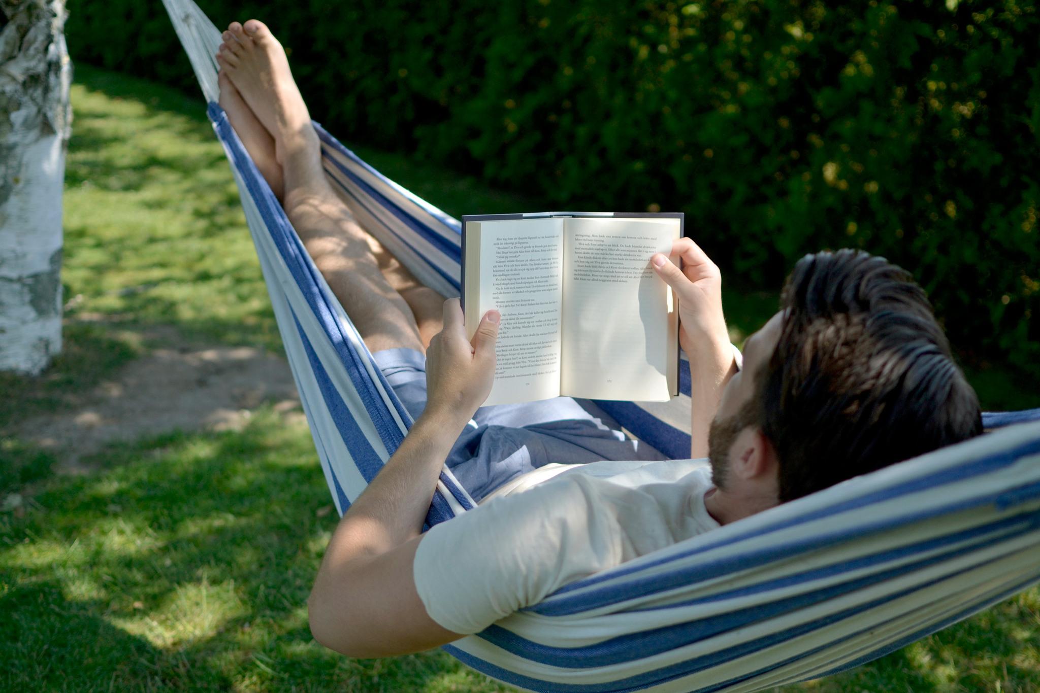 Person lying in a hammock reading a book.