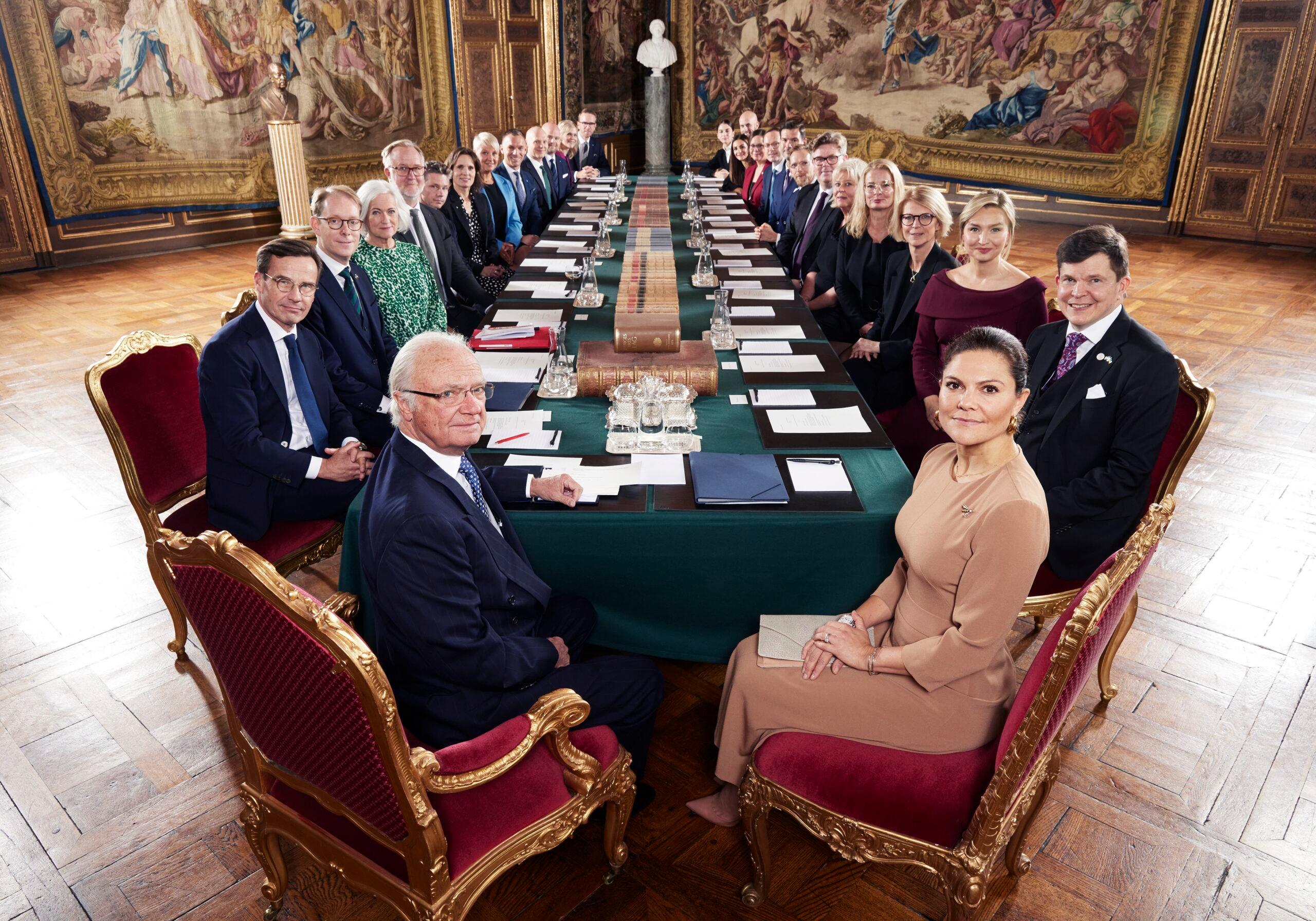 King Carl XVI Gustaf and Crown Princess Victoria seated at a long table with the new Swedish government.  