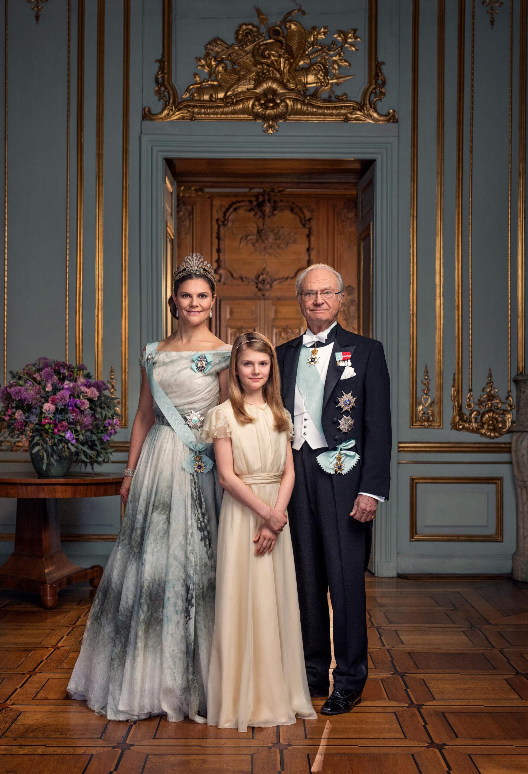 A portrait of Crown Princess Victoria, King Carl XVI Gustaf and Princess Estelle in front of a well-decorated wall and door. 