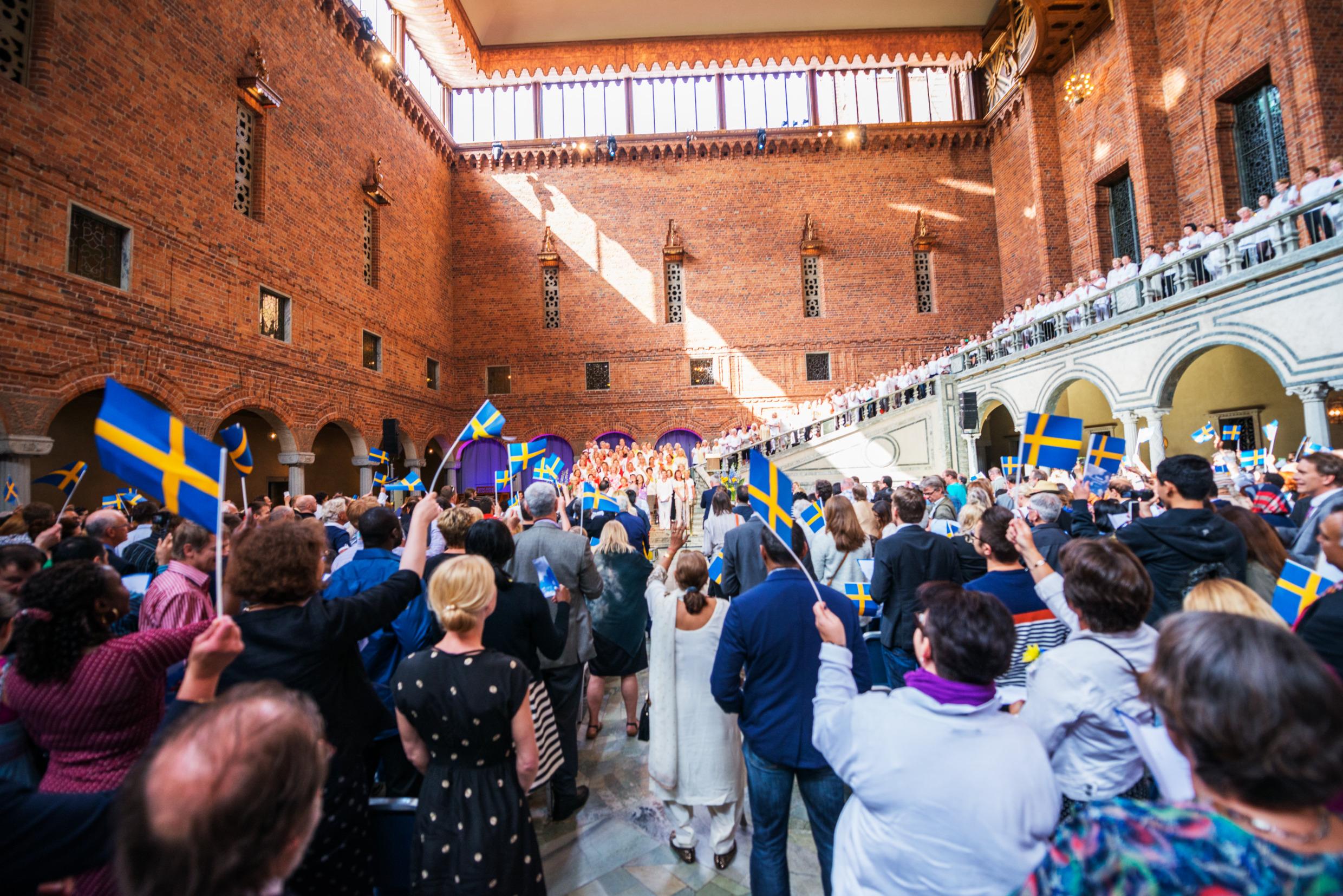 New Swedish citizens pose in the stairs during the welcome ceremony at Stockholm City Hall. They are welcomed by people waving Swedish flags. 