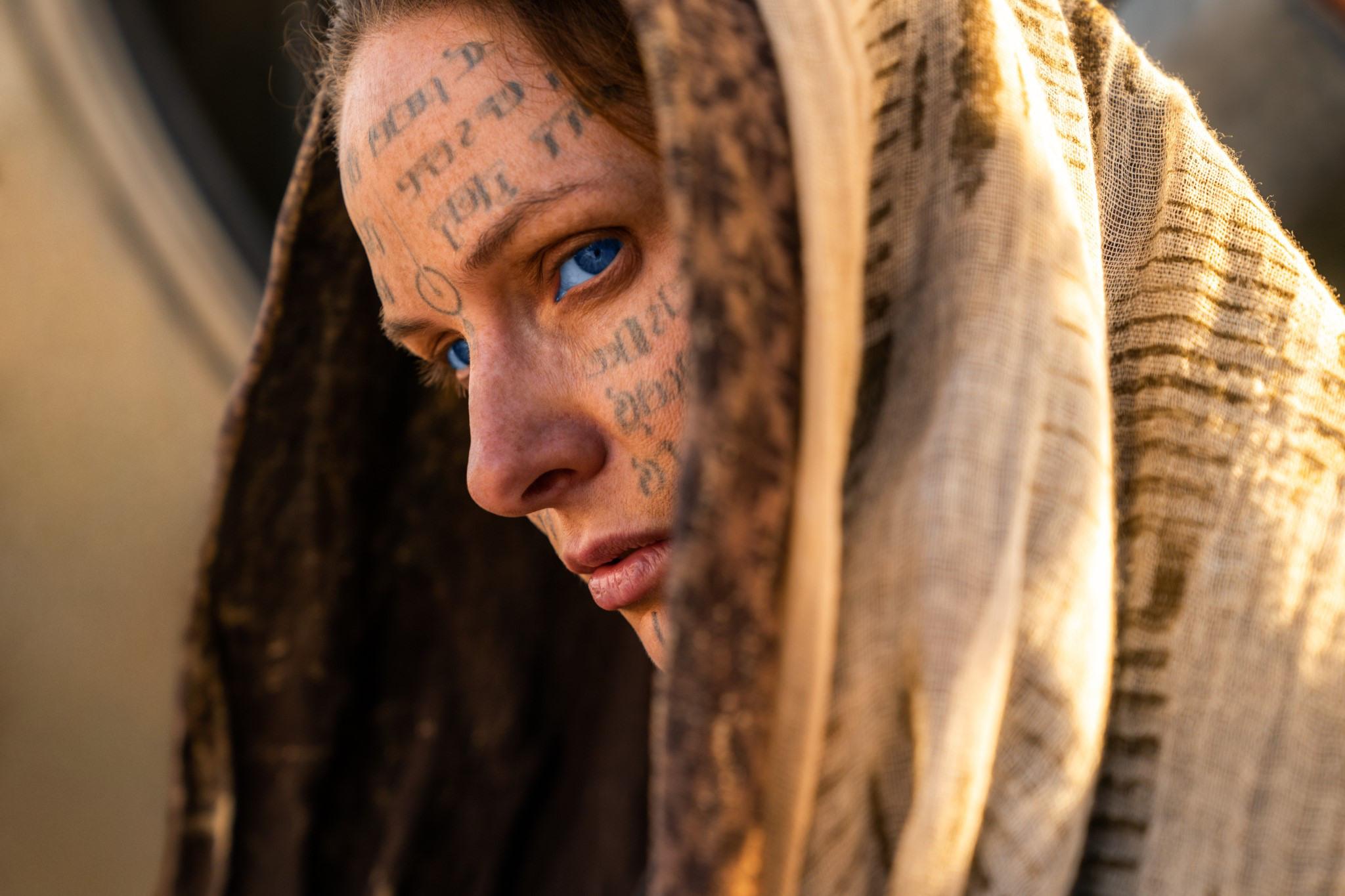 A woman with a shawl on her head and what looks like tatooed letters on her face.