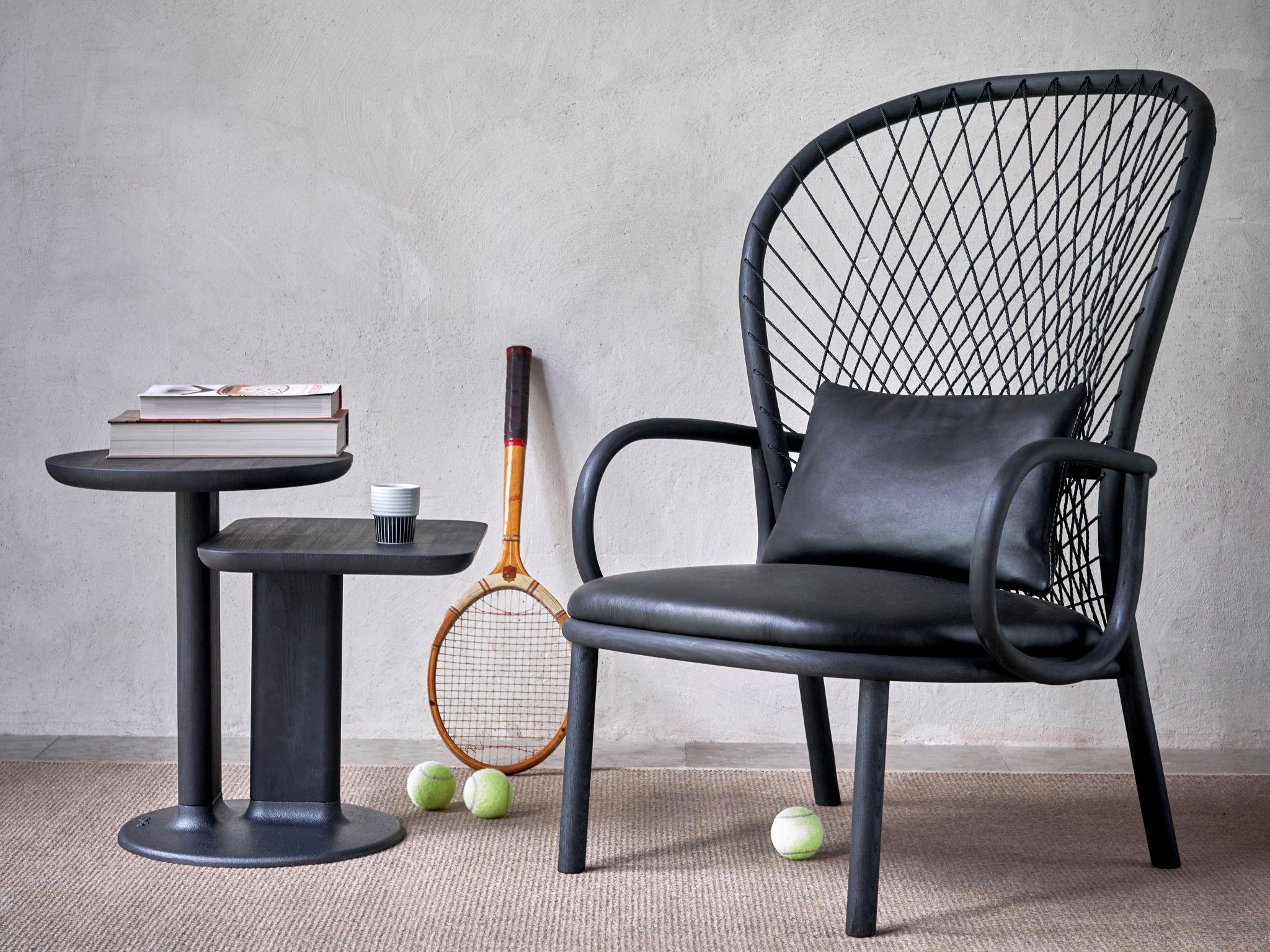 A black armchair next to a table. A tennis racket and balls in the background.