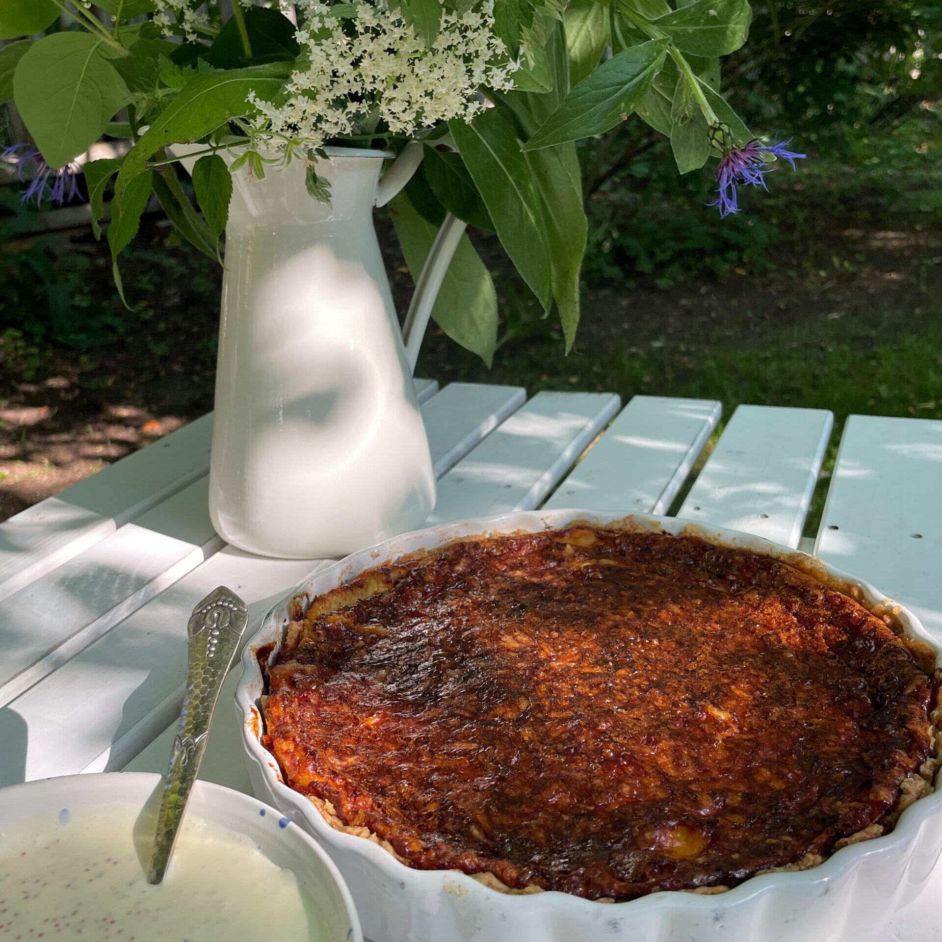 A quiche on a table in front of a vase with flowers.