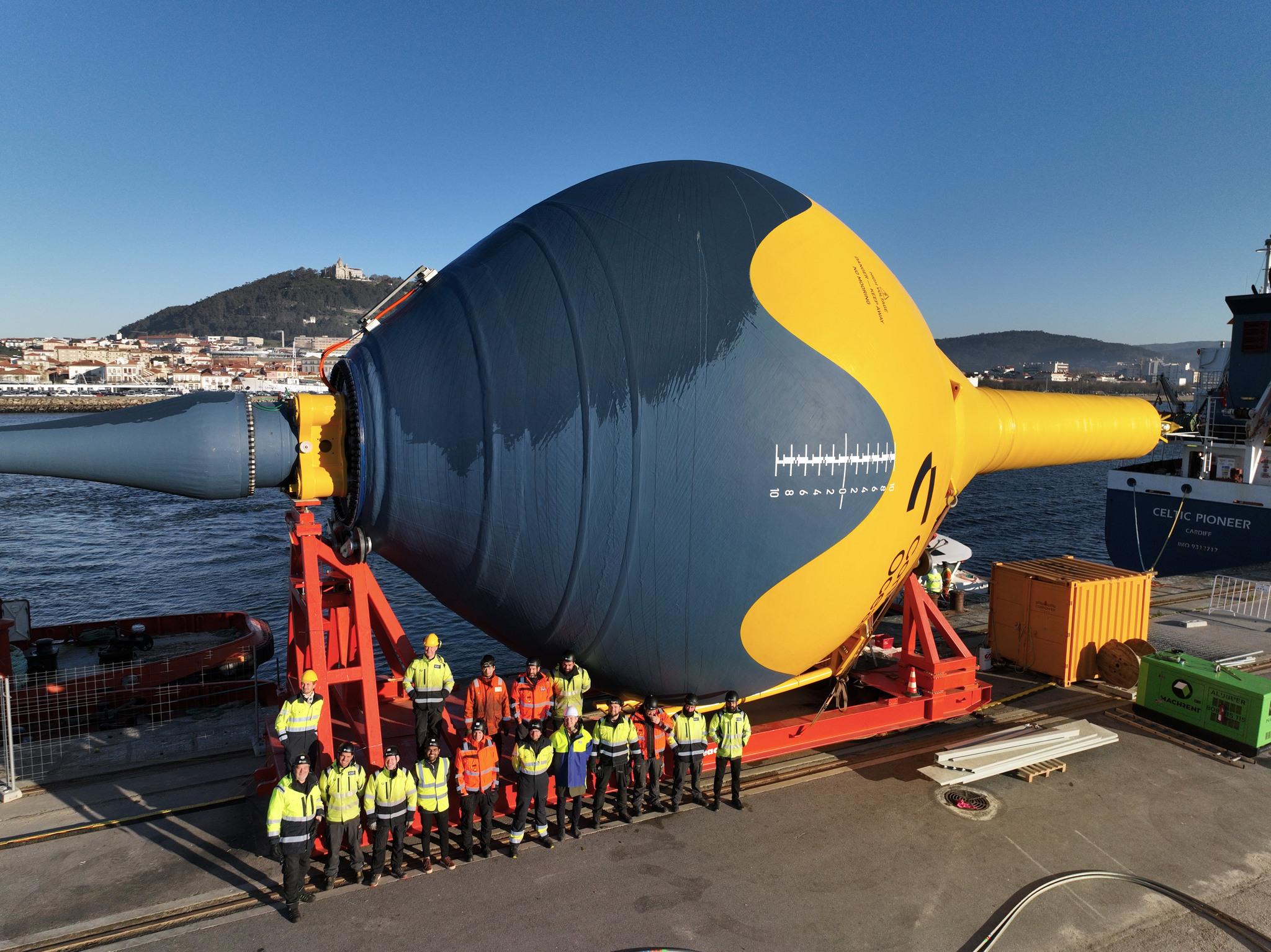 A giant buoy-shaped object lying on a quay with a group of people standing in front of it.