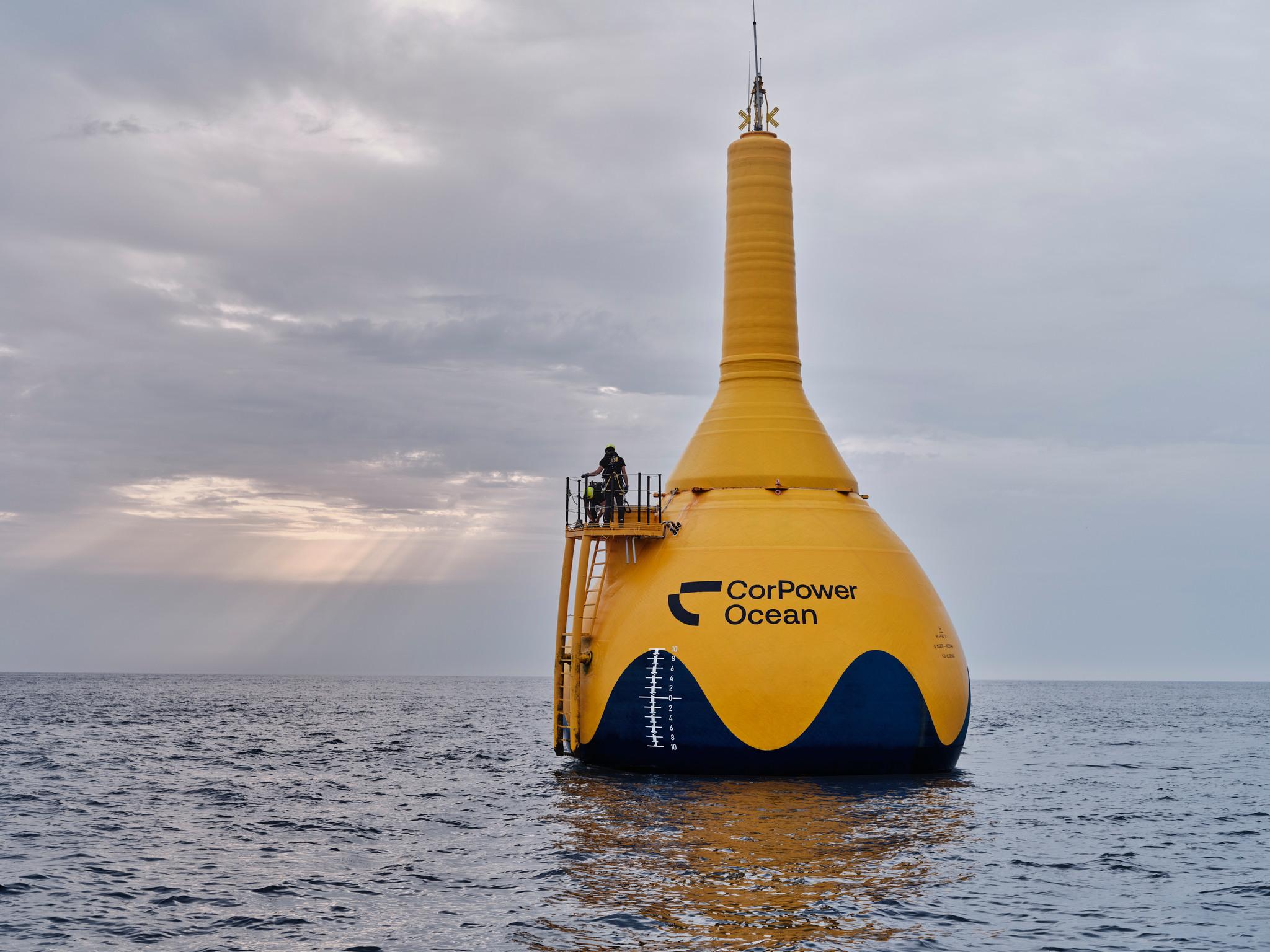 A large, yellow, buoy-shaped object in the water, with a person standing on a platform on its left.