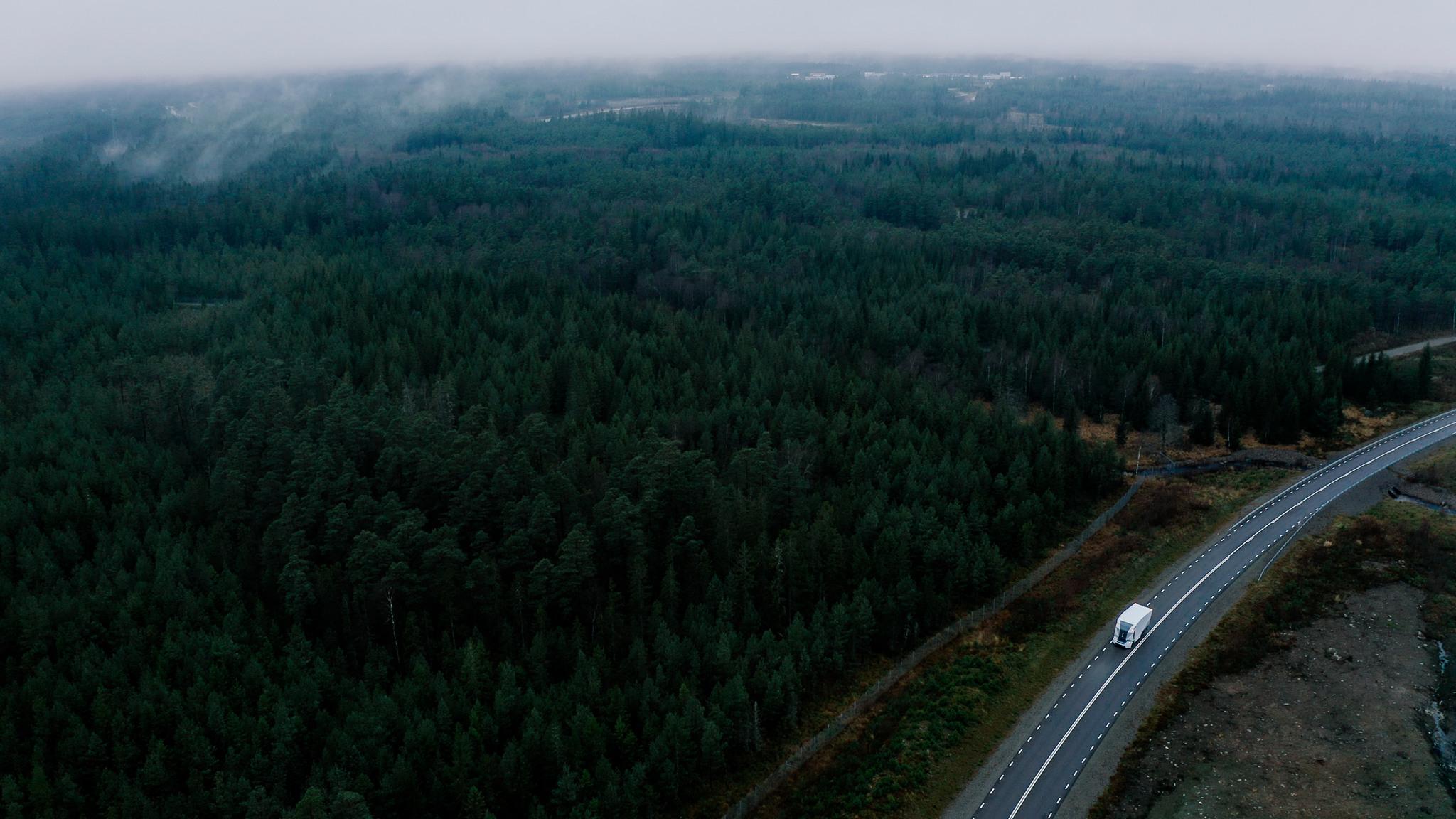 A drone shot of a white lorry on a road surroundes by woods.