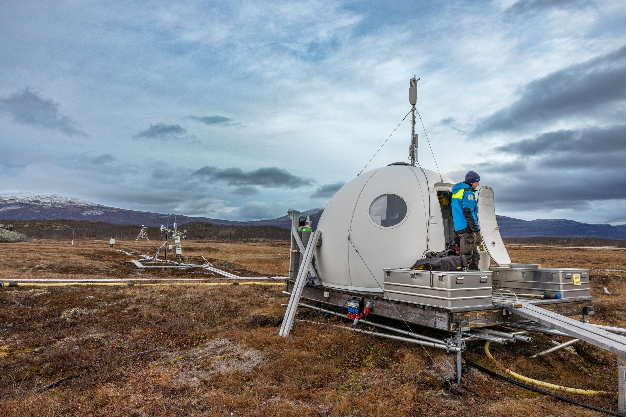 A man stands outside an igloo-looking research station on an arctic tundra.